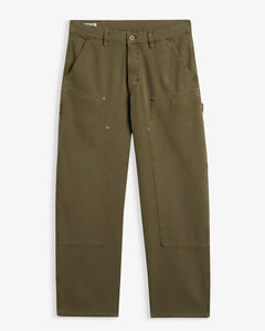 A front view of The Carpenter Pant in olive green, laid flat on a white background. The image highlights the front slash pockets, reinforced knee panels with rivets, and the embroidered c'est normal logo.
