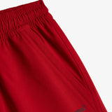 A detailed close-up of The Shorts in red, focusing on the elasticated waistband, side pocket, and the dark c'est normal logo on the leg.