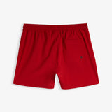 A back view of The Shorts in red, laid flat on a white background. The image highlights the elastic waistband and the back pocket with an eyelet.