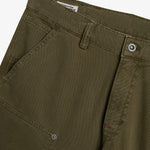 A close-up shot of the front of The Carpenter Pant in olive green, showcasing the textured fabric, a slash pocket, and custom c'est normal buttons and rivets.