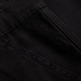 A detailed close-up of The Carpenter Pant in black, highlighting the woven fabric texture, reinforced stitching, and the subtle c'est normal logo.