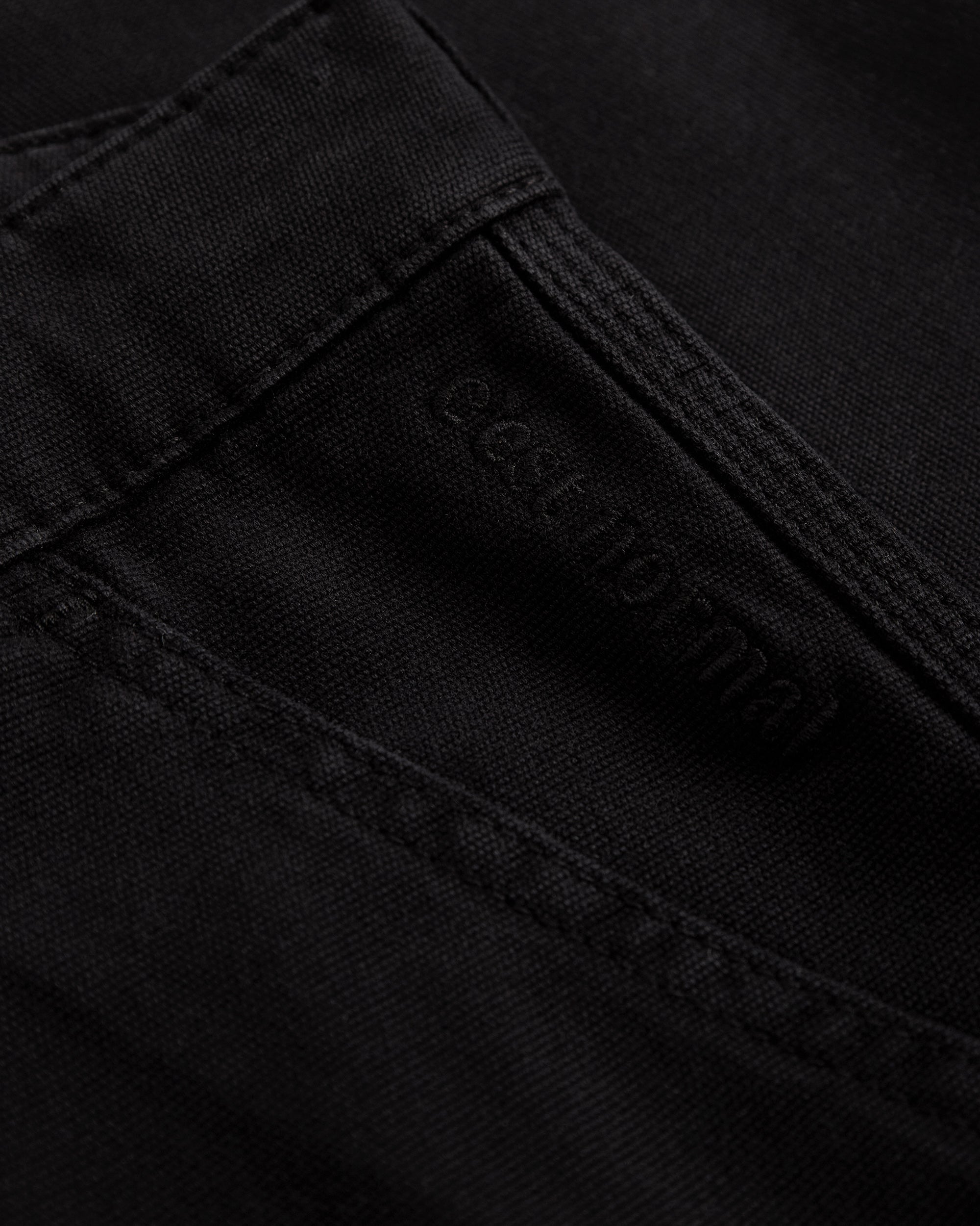 A detailed close-up of The Carpenter Pant in black, highlighting the woven fabric texture, reinforced stitching, and the subtle c'est normal logo.