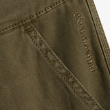 A close-up view of The Carpenter Pant in olive green, focusing on the textured fabric and pocket detailing. The image clearly shows the stitched c'est normal logo near the pocket seam.