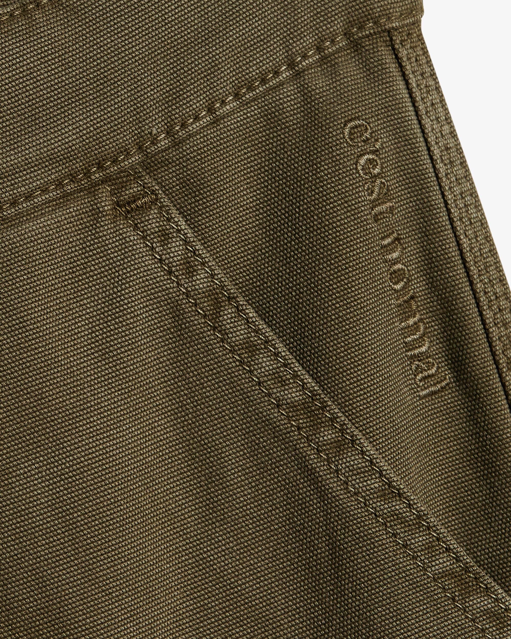A close-up view of The Carpenter Pant in olive green, focusing on the textured fabric and pocket detailing. The image clearly shows the stitched c'est normal logo near the pocket seam.