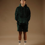 The Oversized Teddy Hoodie in pine — worn as a set with matching shorts and white sneakers