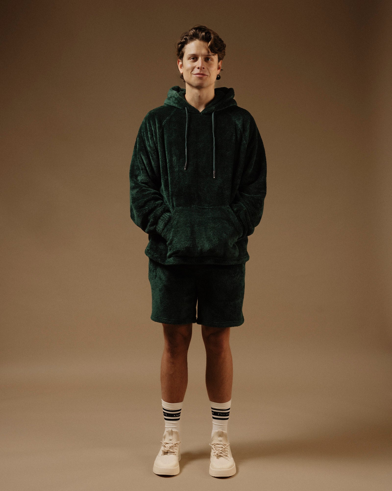 The Oversized Teddy Hoodie in pine — worn as a set with matching shorts and white sneakers