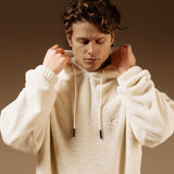 The Oversized Teddy Hoodie in cream — worn by a model adjusting the hood and drawstrings