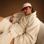 The Oversized Teddy Hoodie in cream — worn with a red and cream cap while lounging