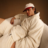 The Oversized Teddy Hoodie in cream — worn with a red and cream cap while lounging