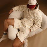 The Oversized Teddy Hoodie in cream — worn with matching shorts in a white textured chair