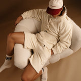 The Oversized Teddy Hoodie in cream — worn with matching shorts in a white textured chair