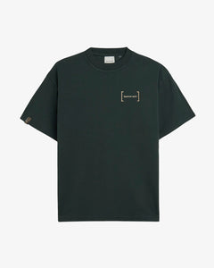 A front view of Le T-Shirt in pine, laid flat on a white background. The image highlights the classic ribbed collar, the slightly oversized fit, the black satin cuff tag, and the FRC edition mirror logo on the chest.