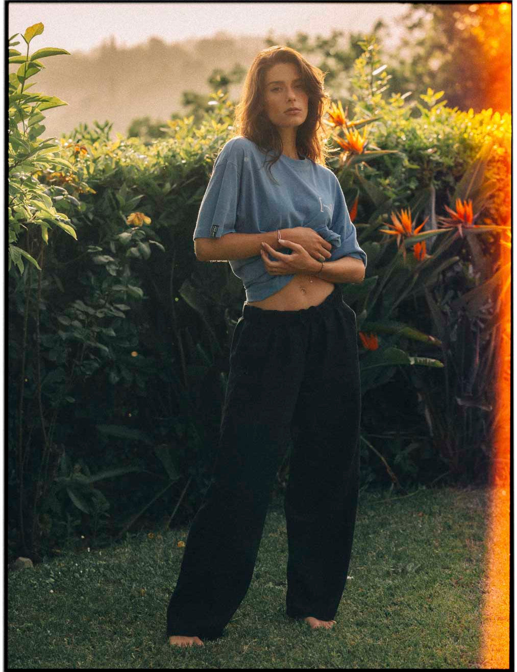 Le Linen T-Shirt in bonnet blue — worn by a woman in a lush garden at sunset
