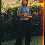 Le Linen T-Shirt in bonnet blue — worn by a woman in a lush garden at sunset
