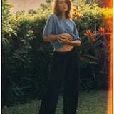 Le Linen T-Shirt in bonnet blue — worn by a woman in a lush garden at sunset