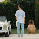 Le Linen T-Shirt in white — back view with C'est normal graphic next to a pool and vintage car