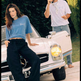 Le Linen T-Shirt in white — worn by a man holding a vintage phone near a classic car