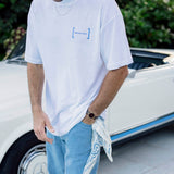 Le Linen T-Shirt in white — worn with blue jeans next to a white vintage car