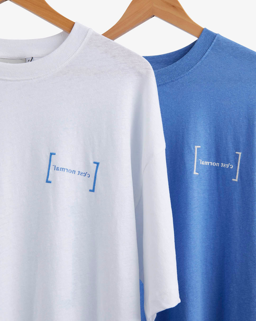 Le Linen T-Shirt in white — hanging next to a blue version with the C'est normal logo