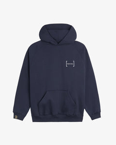 A front view of Le Hoodie in navy, laid flat on a white background. The image highlights the kangaroo front pocket, the white FRC mirror c'est normal logo on the chest, and the signature cuff tag on the sleeve.