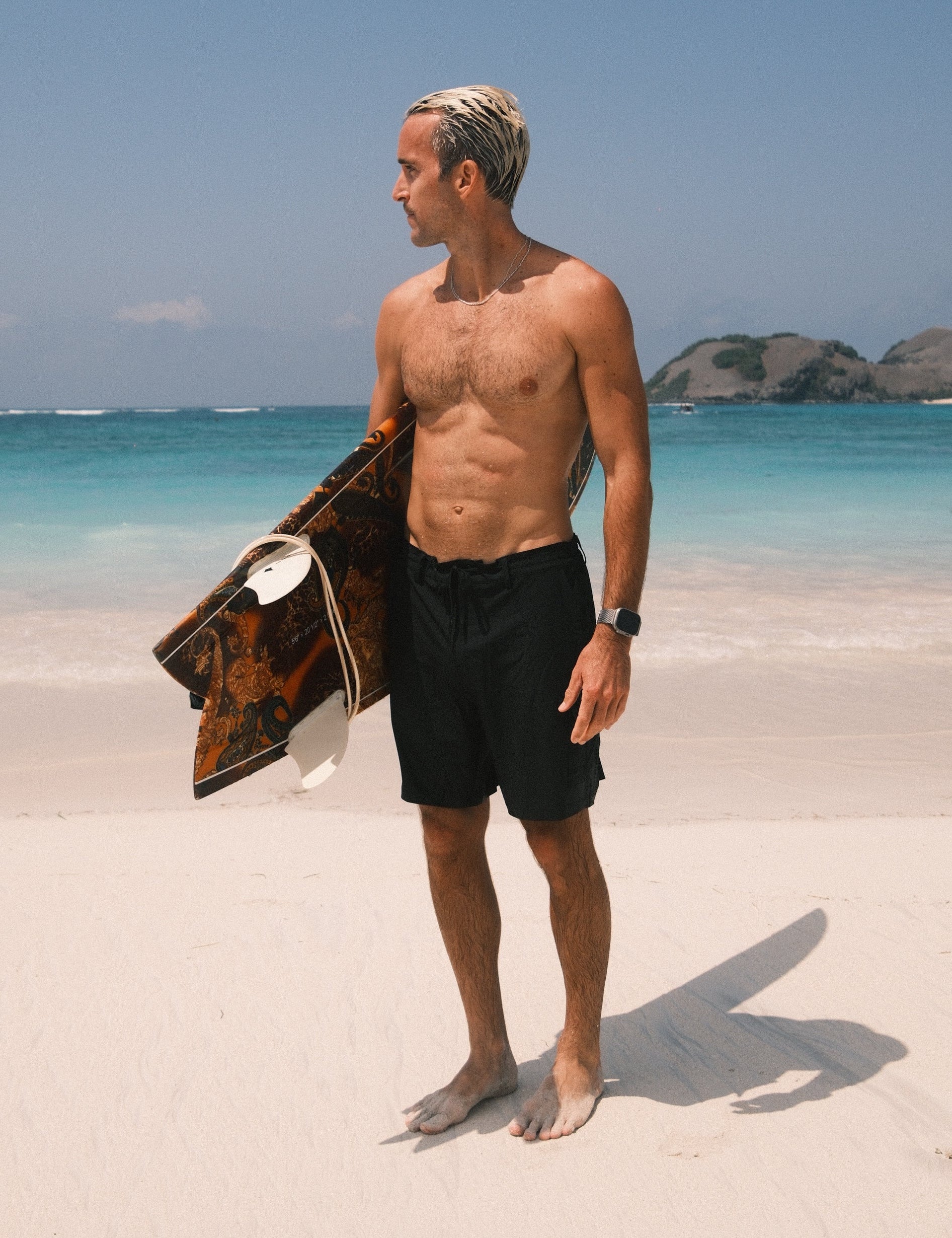 The Board Shorts in black — worn on the beach holding a surfboard