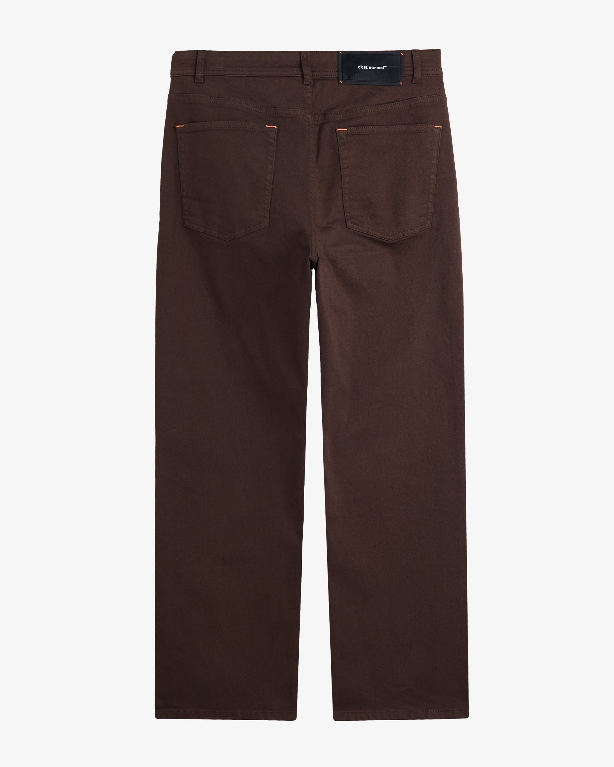 A back view of The 5 Pocket Pants in brown, laid flat on a white background. The image highlights the two back pockets, belt loops, orange accent stitching, and the black rubber patch with the white c'est normal logo.
