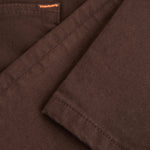A close-up shot of the soft, stretchy denim fabric of The 5 Pocket Pants in brown, highlighting the texture and a touch of orange accent stitching on the pocket.