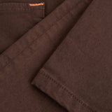 A close-up shot of the soft, stretchy denim fabric of The 5 Pocket Pants in brown, highlighting the texture and a touch of orange accent stitching on the pocket.