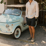 The Board Shorts in khaki — worn with a white linen shirt next to a vintage light blue car