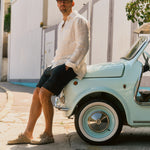 The Board Shorts in black — worn with a white linen shirt while leaning on a vintage car
