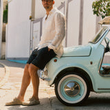 The Board Shorts in black — worn with a white linen shirt while leaning on a vintage car
