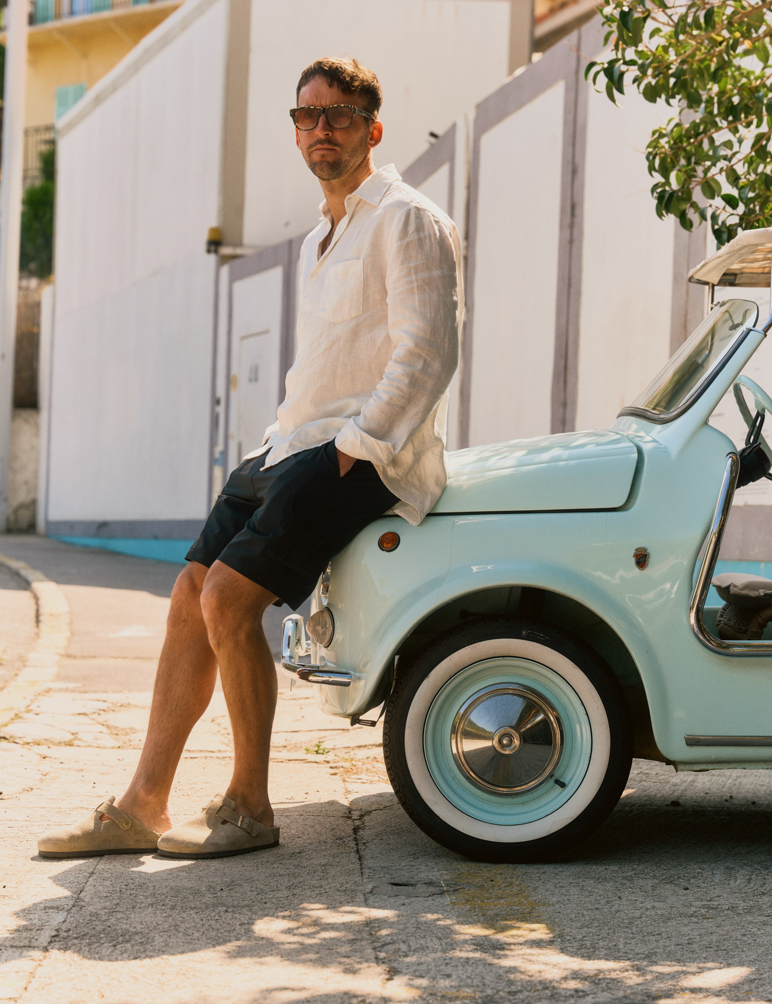 The Board Shorts in black — worn with a white linen shirt while leaning on a vintage car