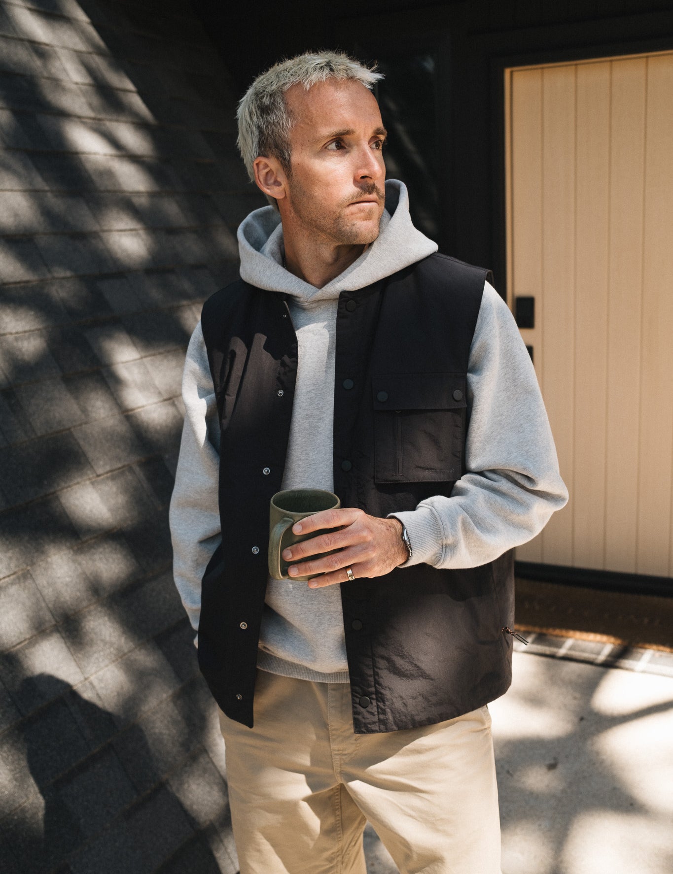 The Utility Vest in black — worn over a grey hoodie outdoors