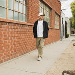 The Monterey Cargo Pant in light khaki — worn while walking along a red brick building