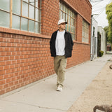 The Monterey Cargo Pant in light khaki — worn while walking along a red brick building