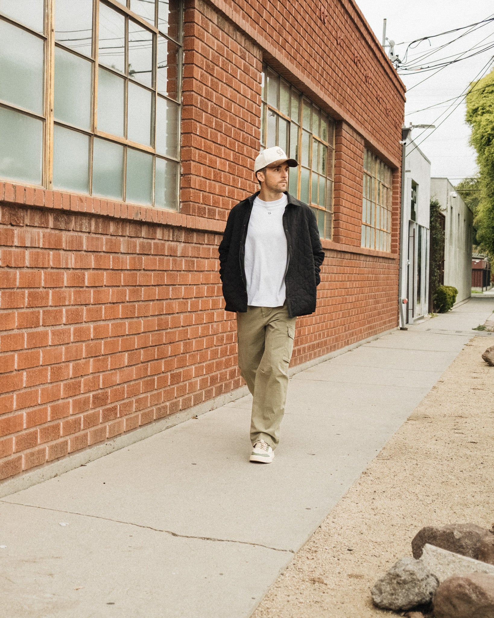 The Monterey Cargo Pant in light khaki — worn while walking along a red brick building