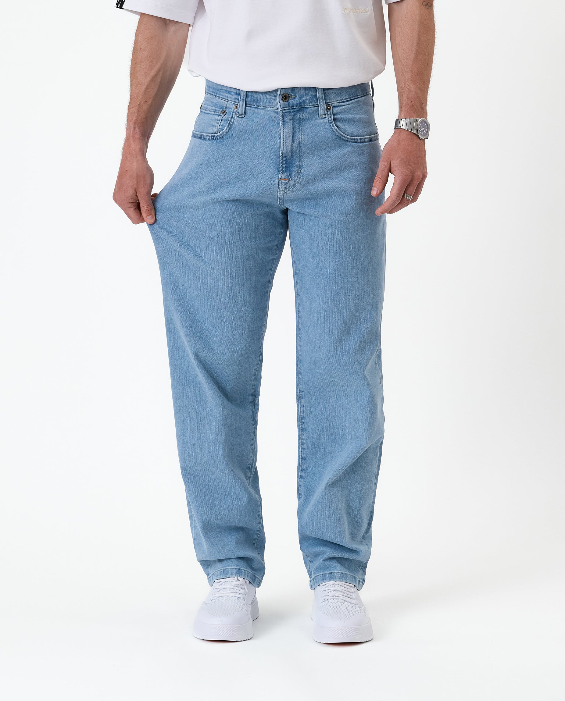 The Jeans Relaxed Straight Fit in light blue — hand pulling the fabric to show stretch