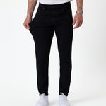 The Jeans Skinny Fit in jet black — pulling at the thigh to show the fabric's stretch