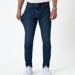 The Jeans Skinny Fit in midwash — fabric being pulled to demonstrate stretch