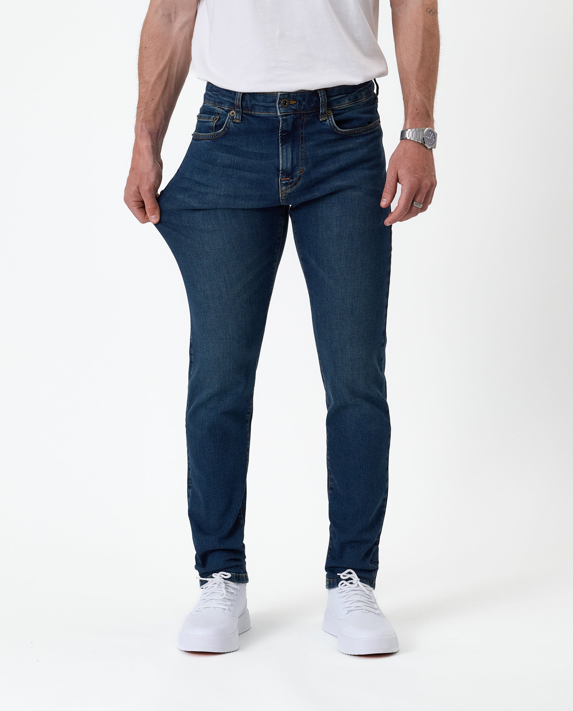 The Jeans Skinny Fit in midwash — fabric being pulled to demonstrate stretch