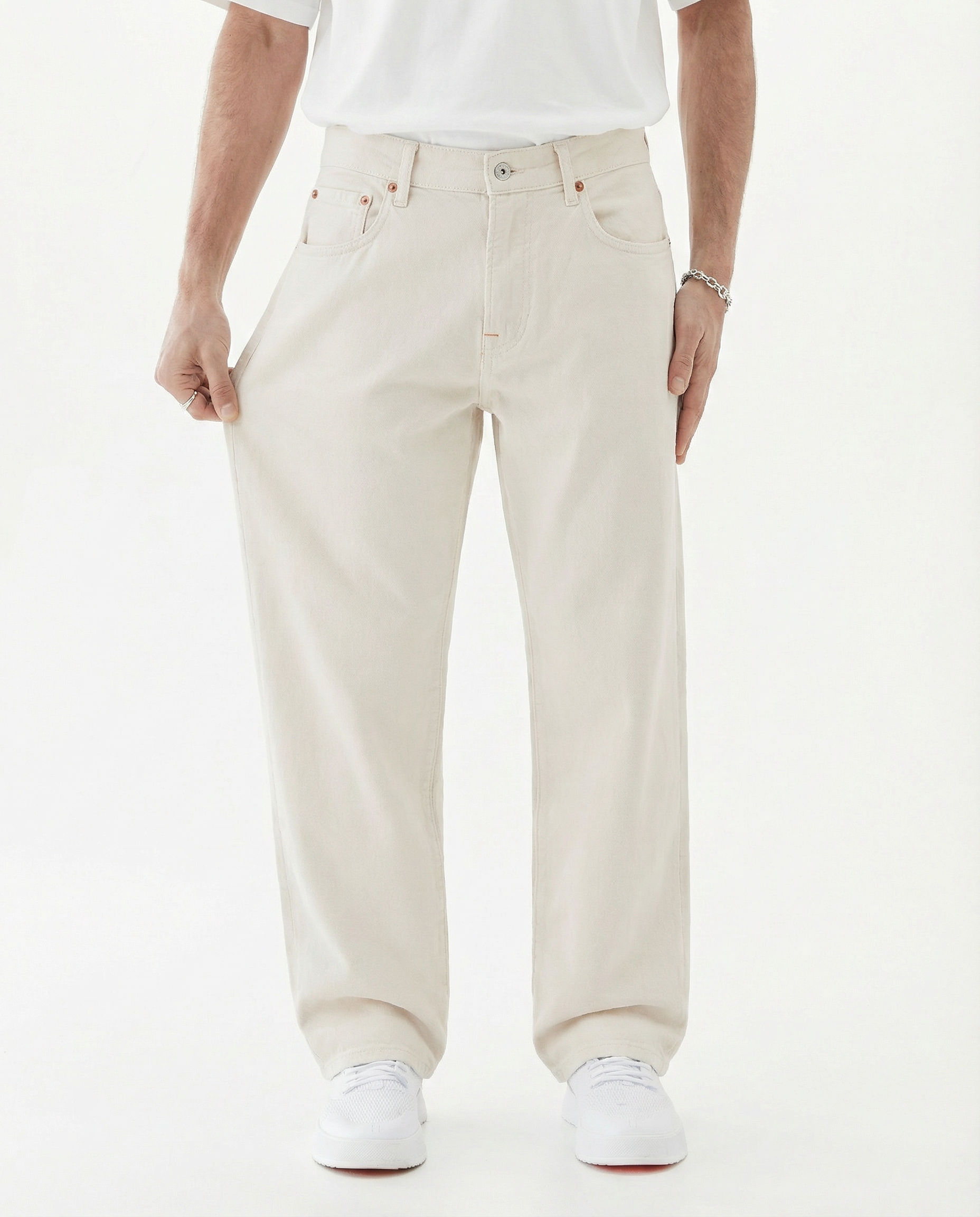 The Jeans Relaxed Straight Fit in ecru — model pulling at the leg to show fabric stretch