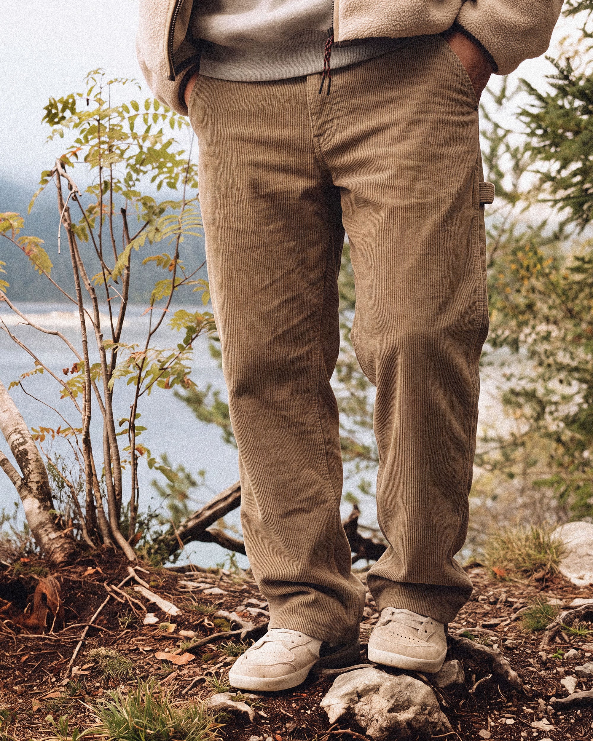 The Lille Cord Carpenter Pant in dark sand — worn outdoors with white sneakers