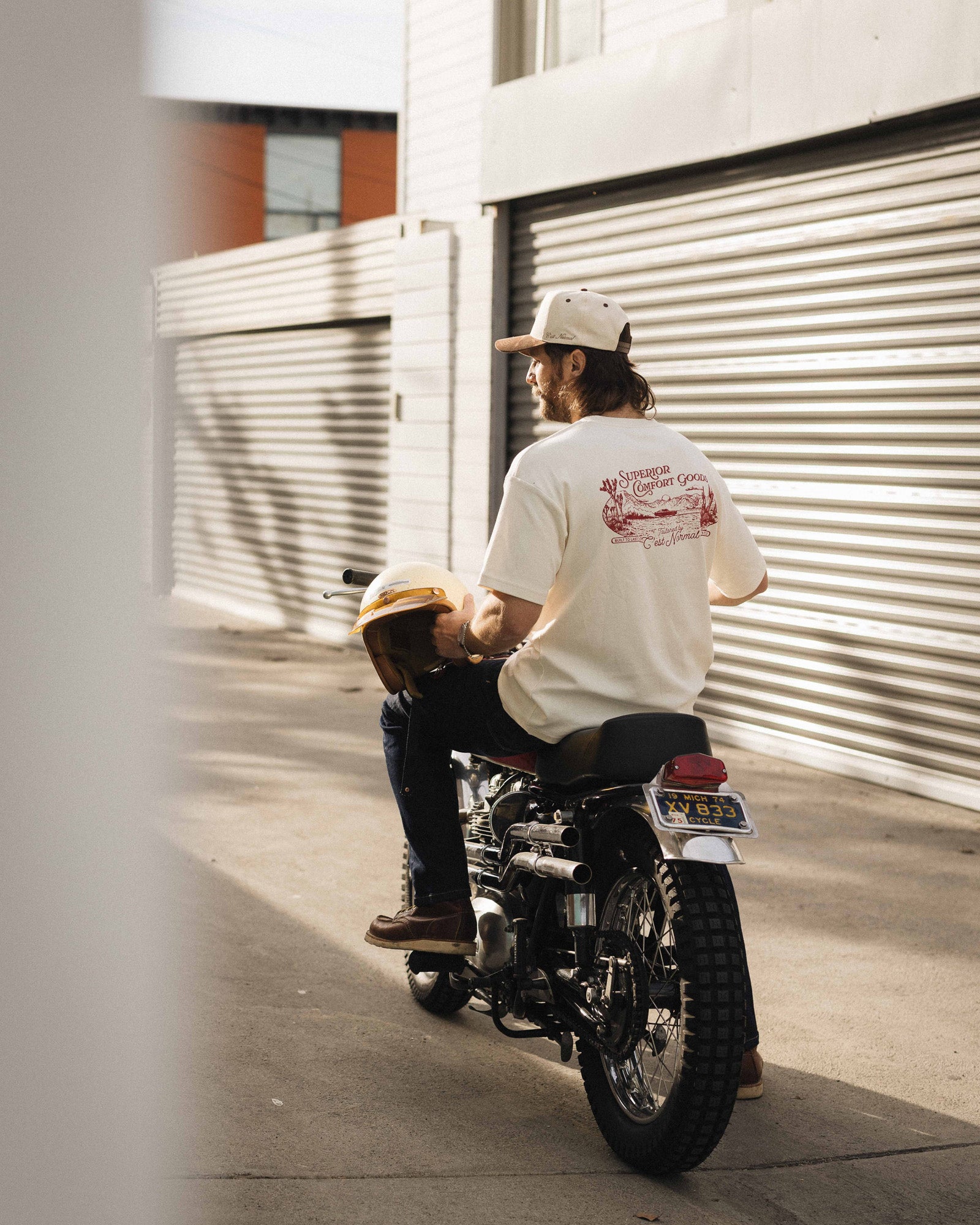 The Oversized Printed T-shirt in cream/black — worn on a motorcycle showing the back print