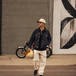 The Jeans Relaxed Straight Fit in ecru — worn with a denim jacket and holding a helmet