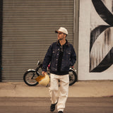 The Jeans Relaxed Straight Fit in ecru — worn with a denim jacket and holding a helmet