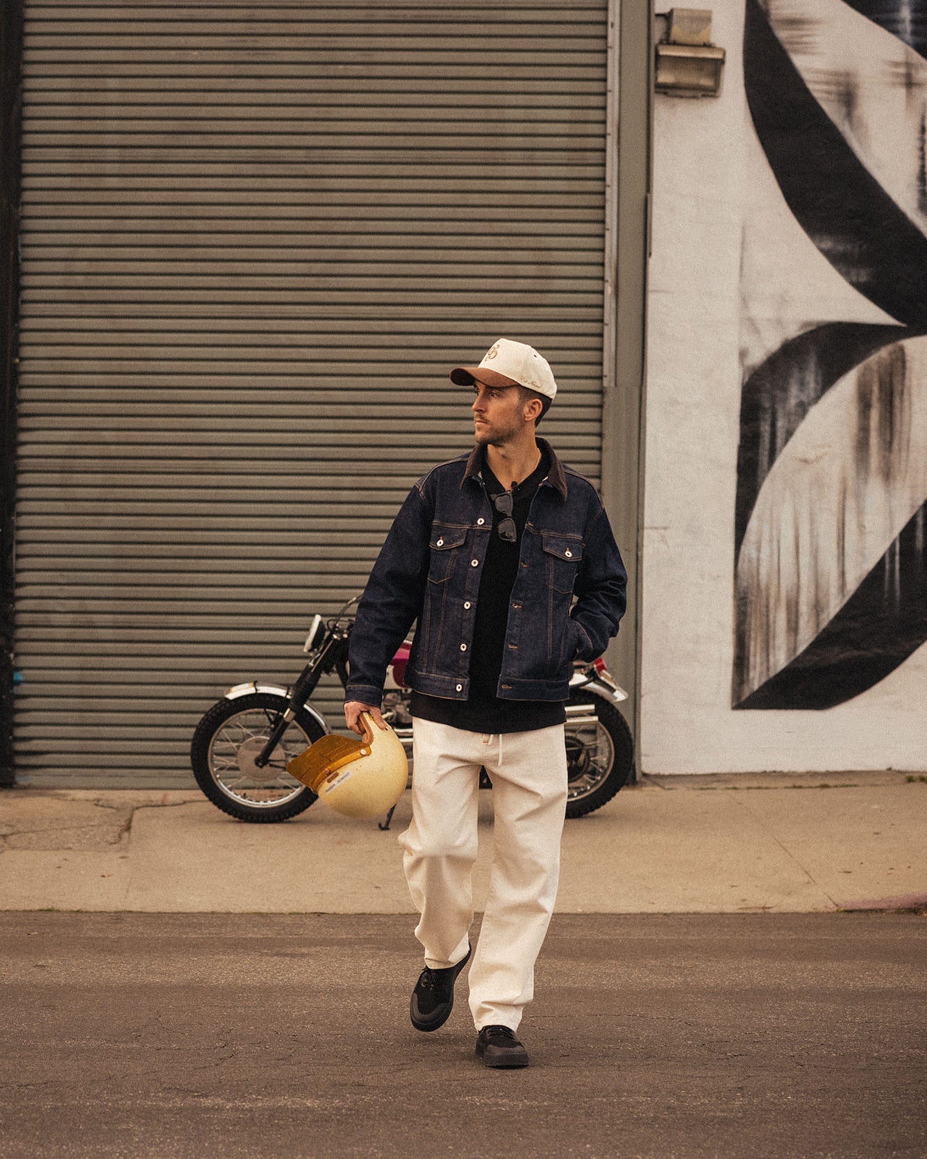 The Jeans Relaxed Straight Fit in ecru — worn with a denim jacket and holding a helmet