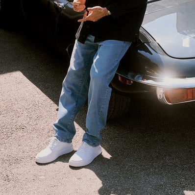 The Jeans Relaxed Straight Fit in light blue — leaning against a black vintage car