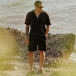 The Holiday Linen Short in black — worn with a matching linen shirt by the sea