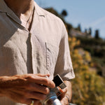 The Holiday Linen SS Shirt in natural — worn while holding a vintage camera