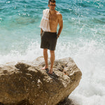 The Board Shorts in khaki — worn while standing on a rock with crashing waves